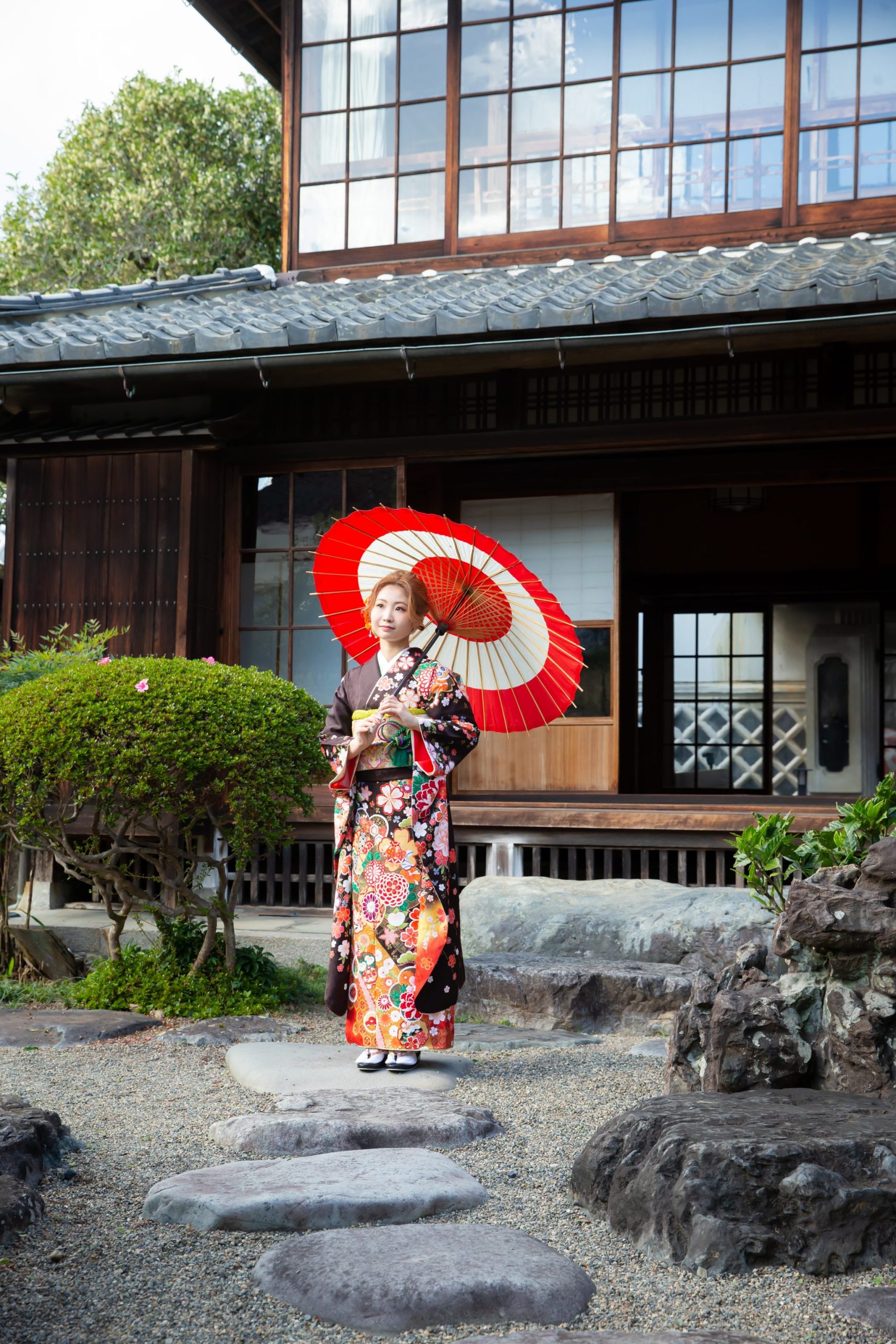 和傘を持って日本庭園に立つ振り袖姿の女性