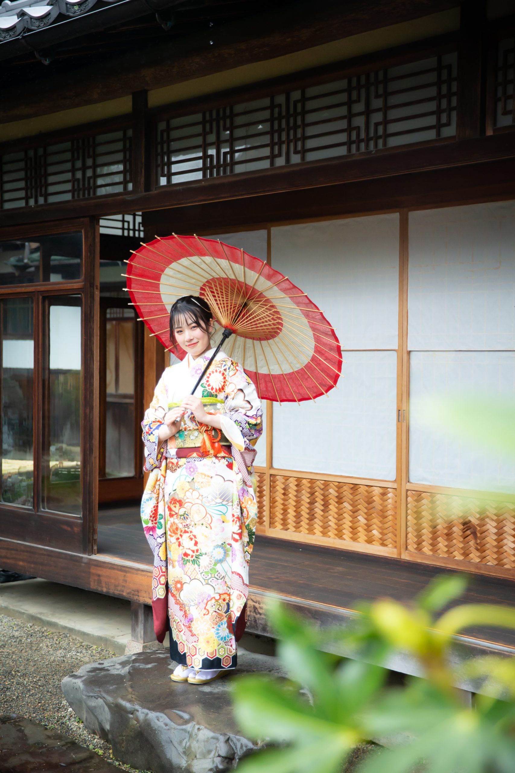 沓脱石の上に和傘をさして立つ振袖姿の女性