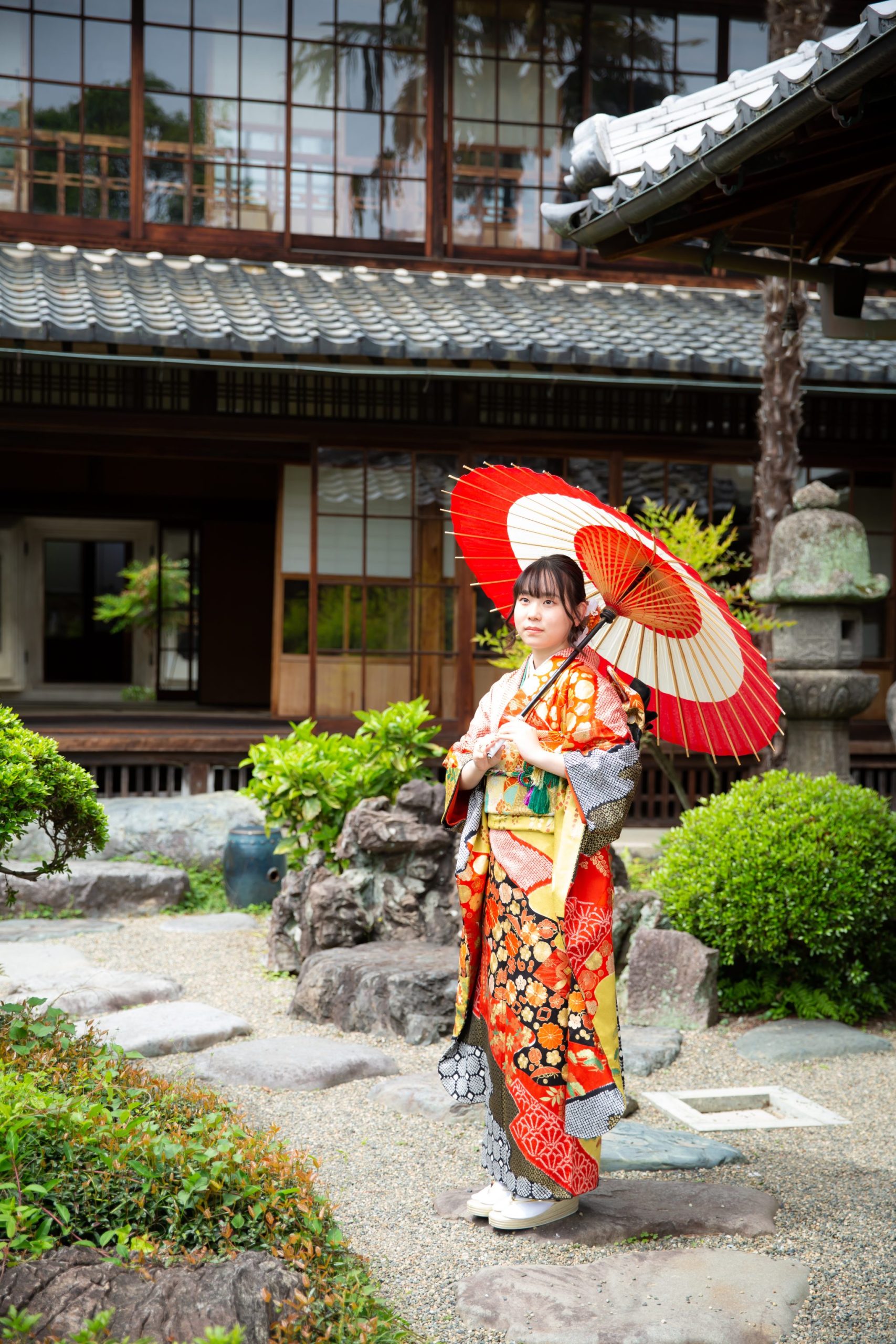 日本庭園で和傘をさして立つ振袖姿の女性