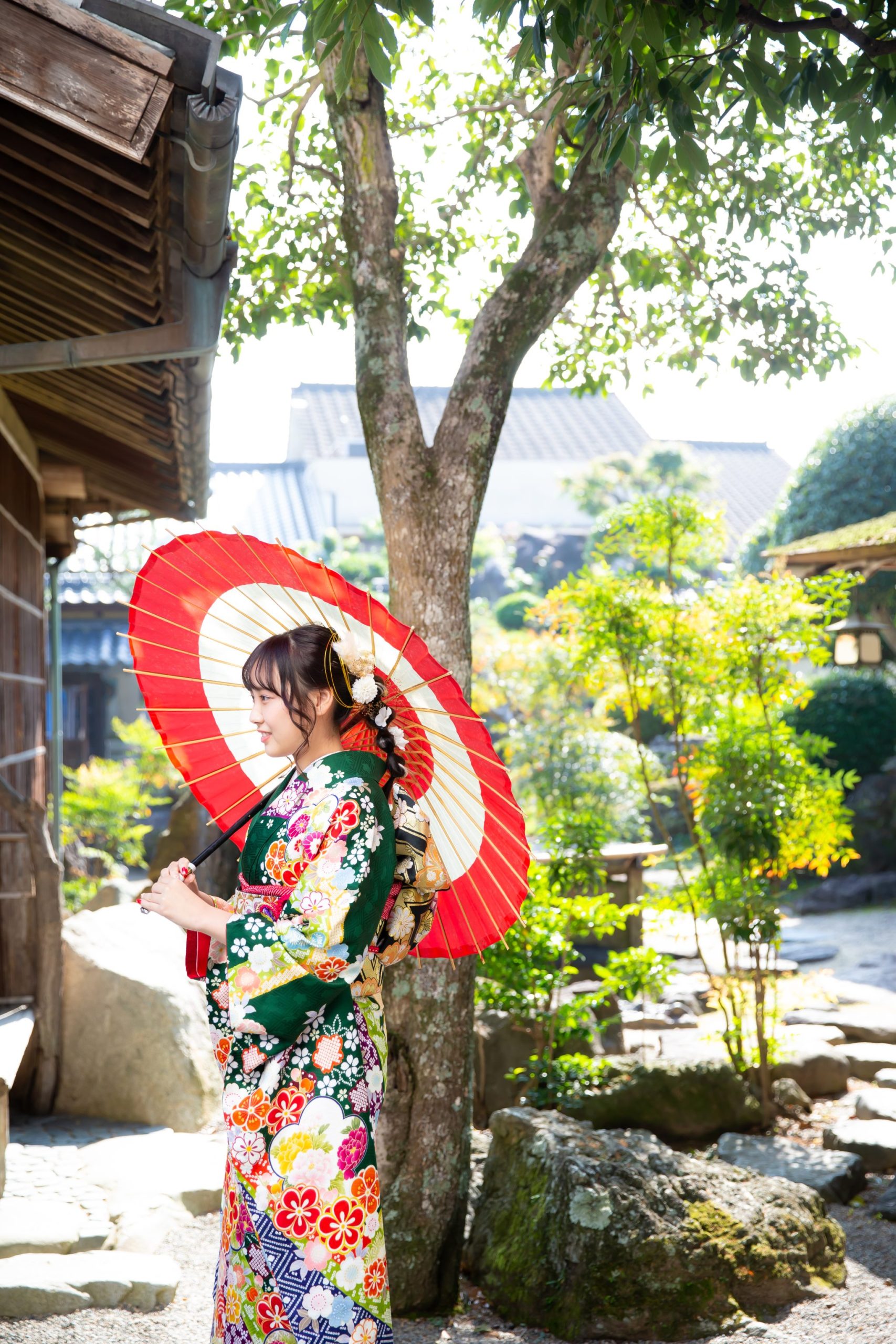 日本庭園で和傘をさす緑の振袖を着た女性