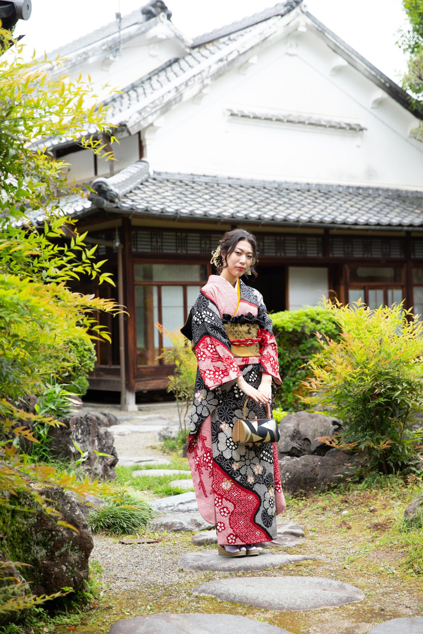 赤と黒の振袖を着て日本庭園に立つ女性