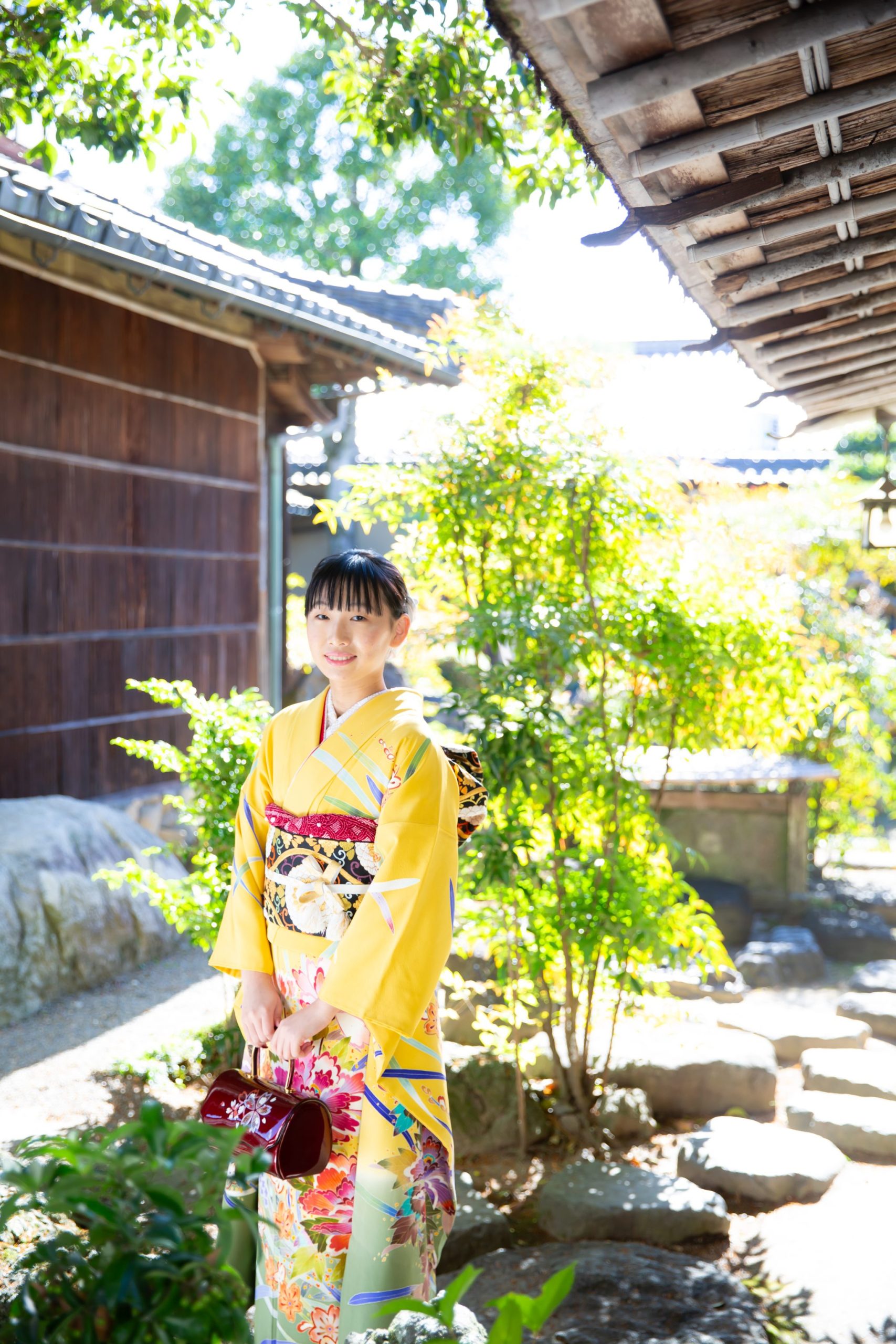 黄色の振袖を着て日本庭園に立つ女性