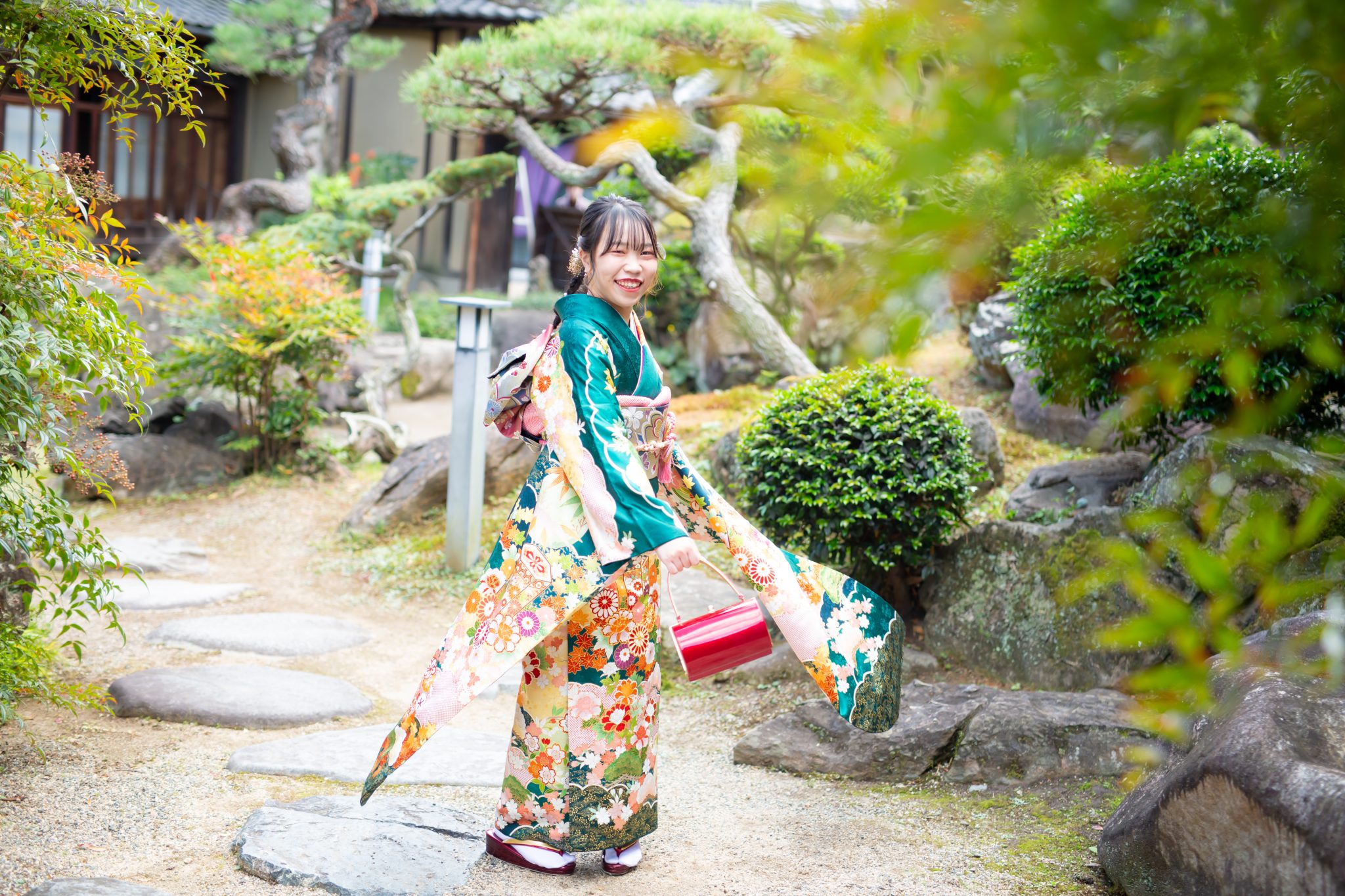 緑の振袖を着て、日本庭園で振り向く若い女性