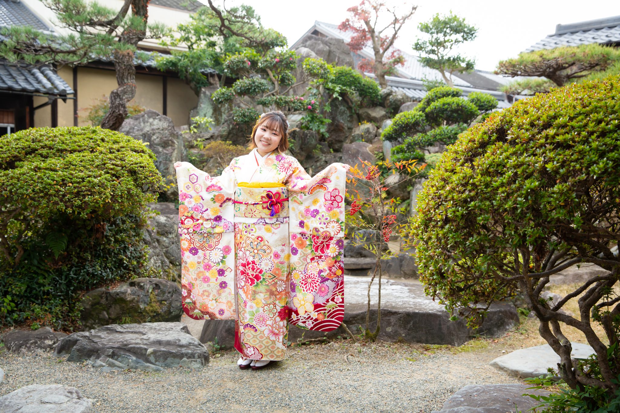 白とピンクの振袖姿で日本庭園に立つ女性